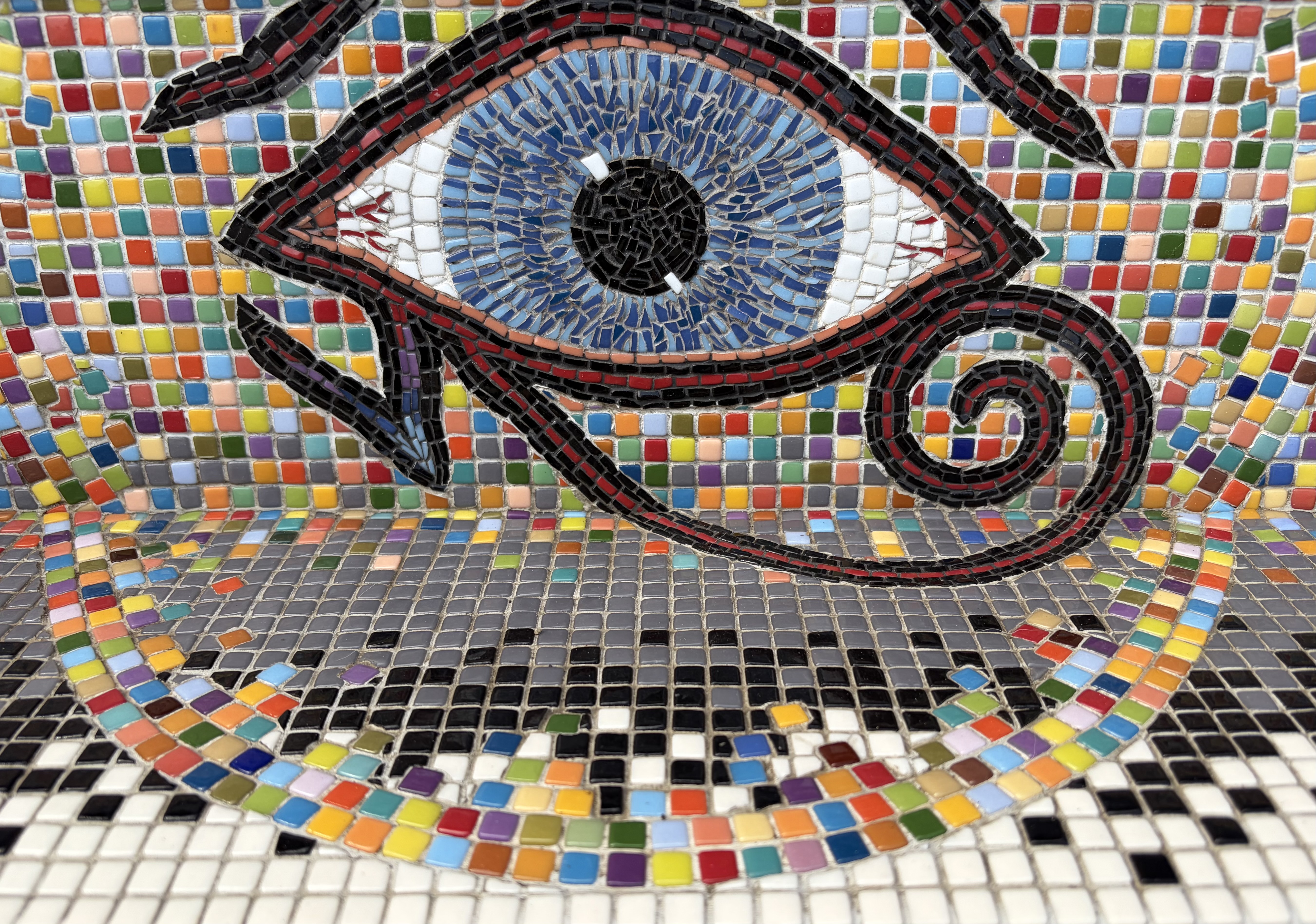 Close-up detail of the Eye of Horus mosaic, showing the blue iris, black pupil, and red-and-black spiral against a rainbow tessellated ground