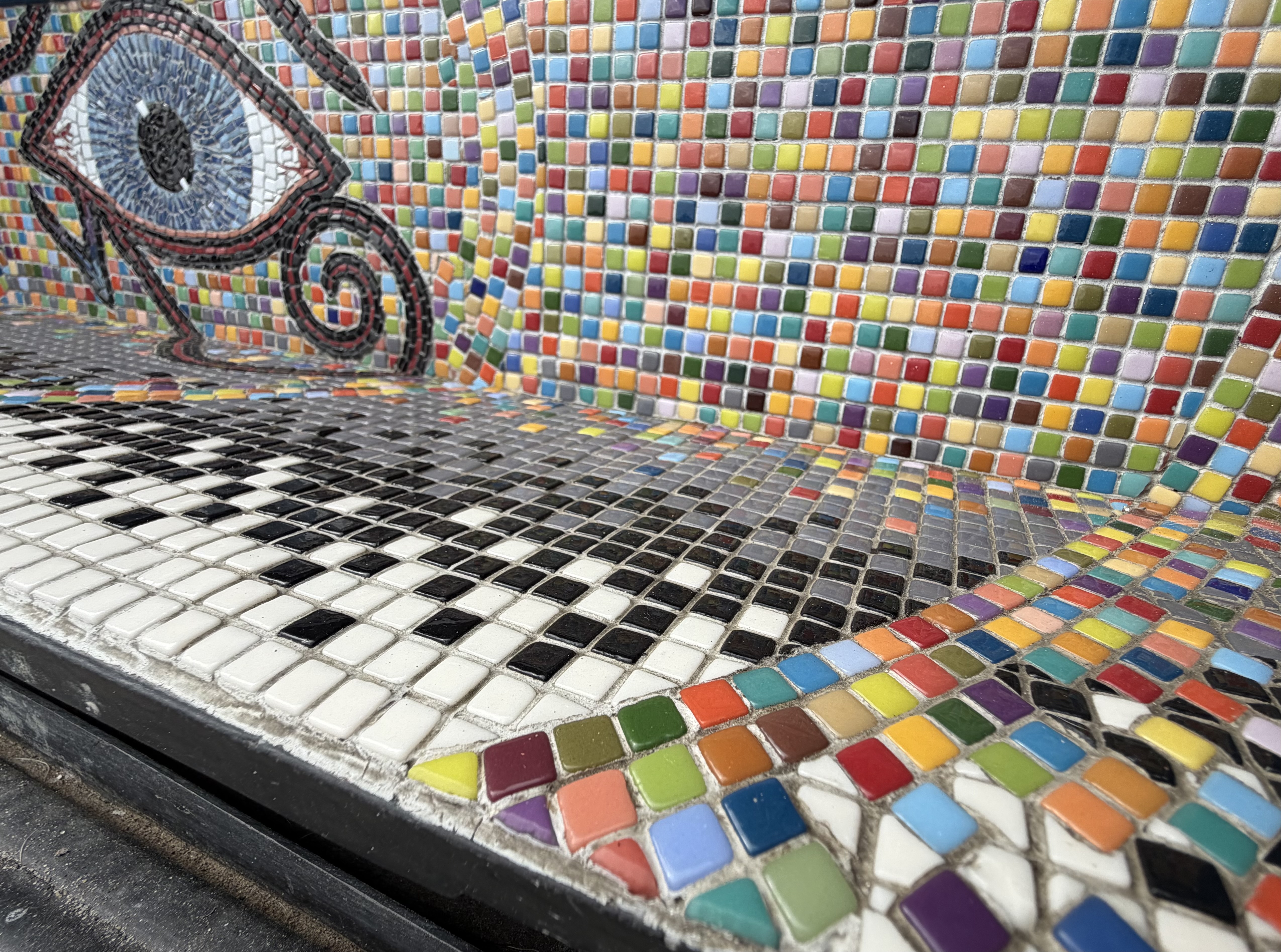 Angled bench view of the Eye of Horus beside a black, white, and rainbow tile grid
