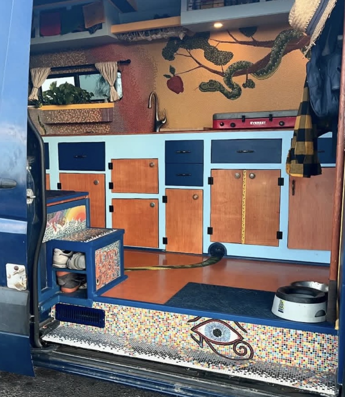 Full view of the van kitchen showing both the Deception serpent mosaic above and the Attention eye mosaic on the bench below
