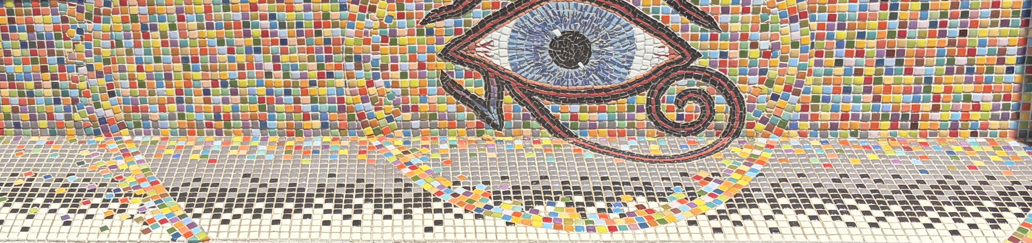 Wide view of the Attention mosaic, an Eye of Horus in blue and black glass tesserae against a rainbow tile ground, with a colorful serpentine ribbon trailing across the bench below
