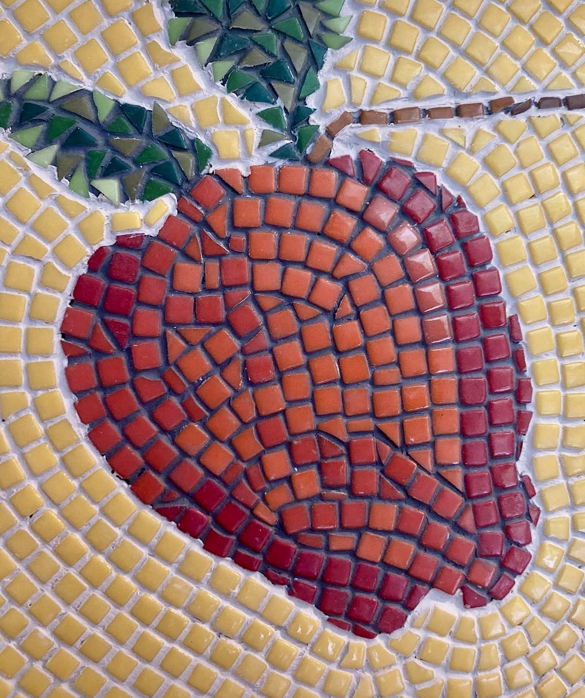Close-up detail of the mosaic apple in red and orange glass tesserae, with a leafy green branch above it