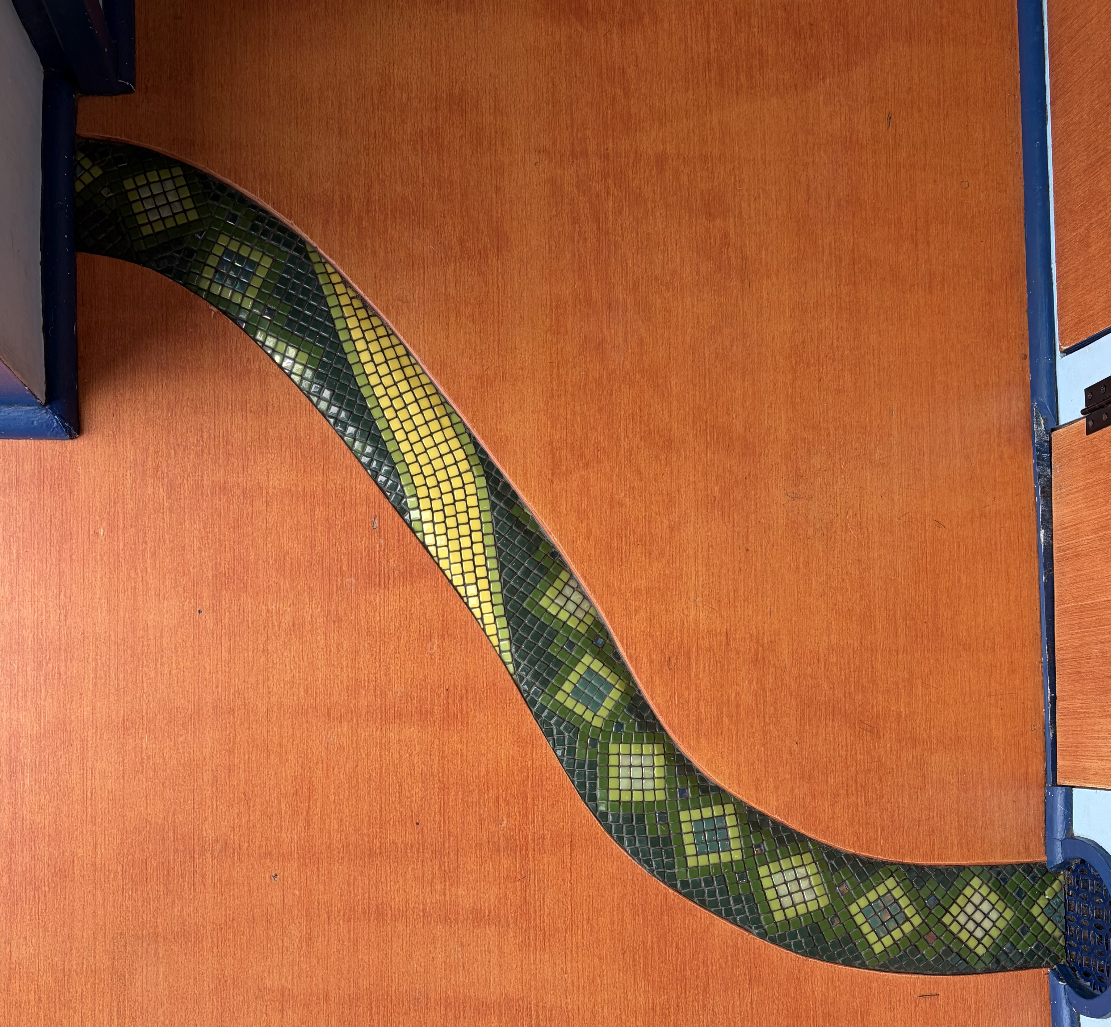 S-curved mosaic snake trim in green and yellow glass tesserae along a wood cabinet edge