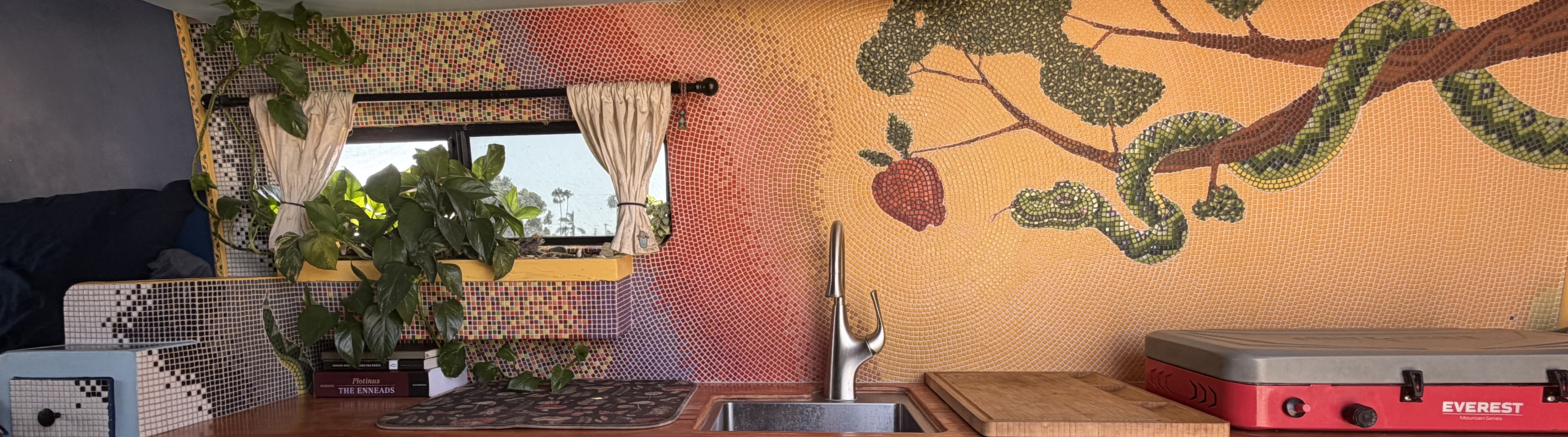Wide panorama of the Deception mosaic installed in a van kitchen, showing the full serpent, branch, and apple against an orange-to-yellow gradient ground