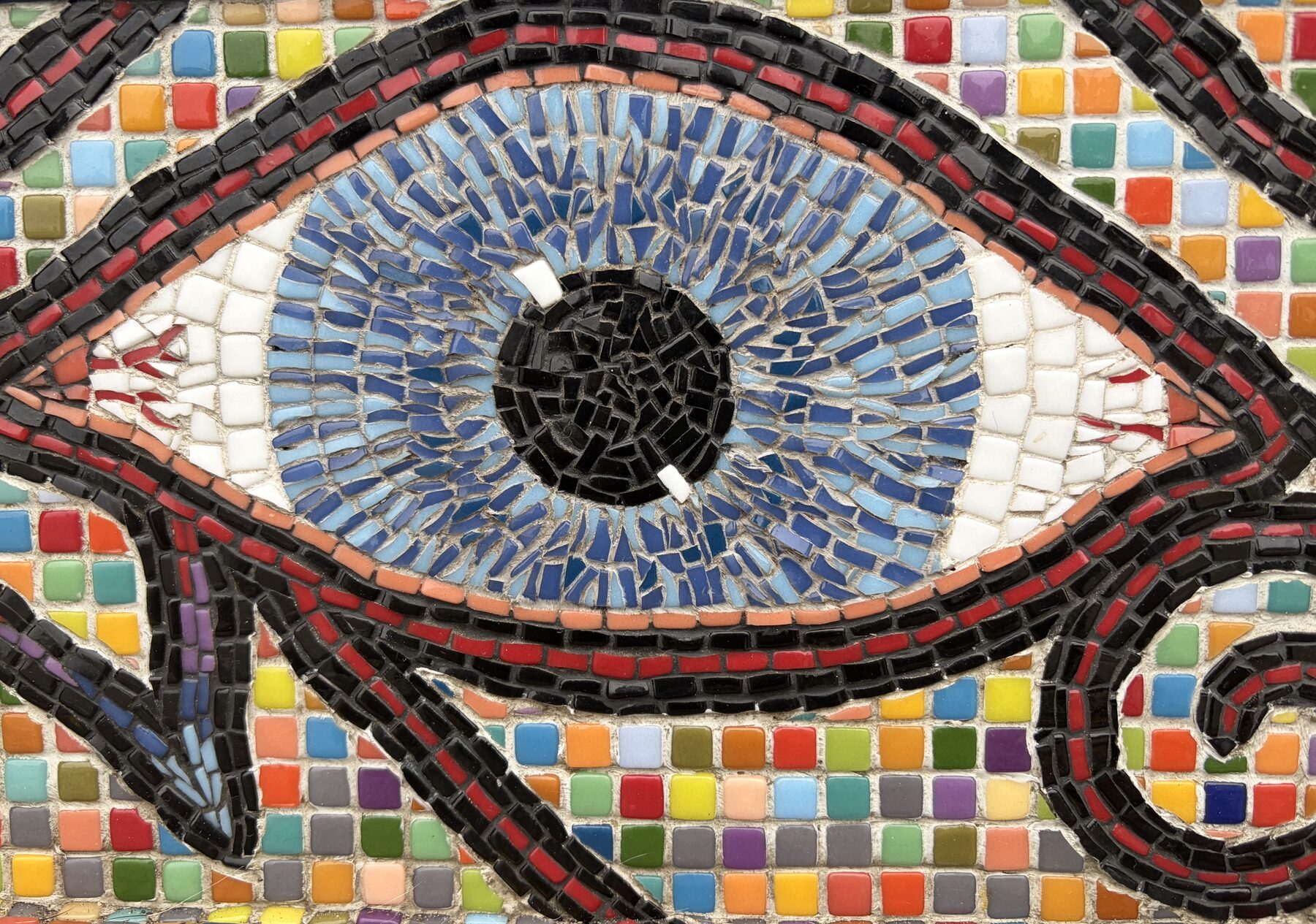 Detail of a mosaic eye, rendered in blue and white tesserae with a border of rainbow tiles