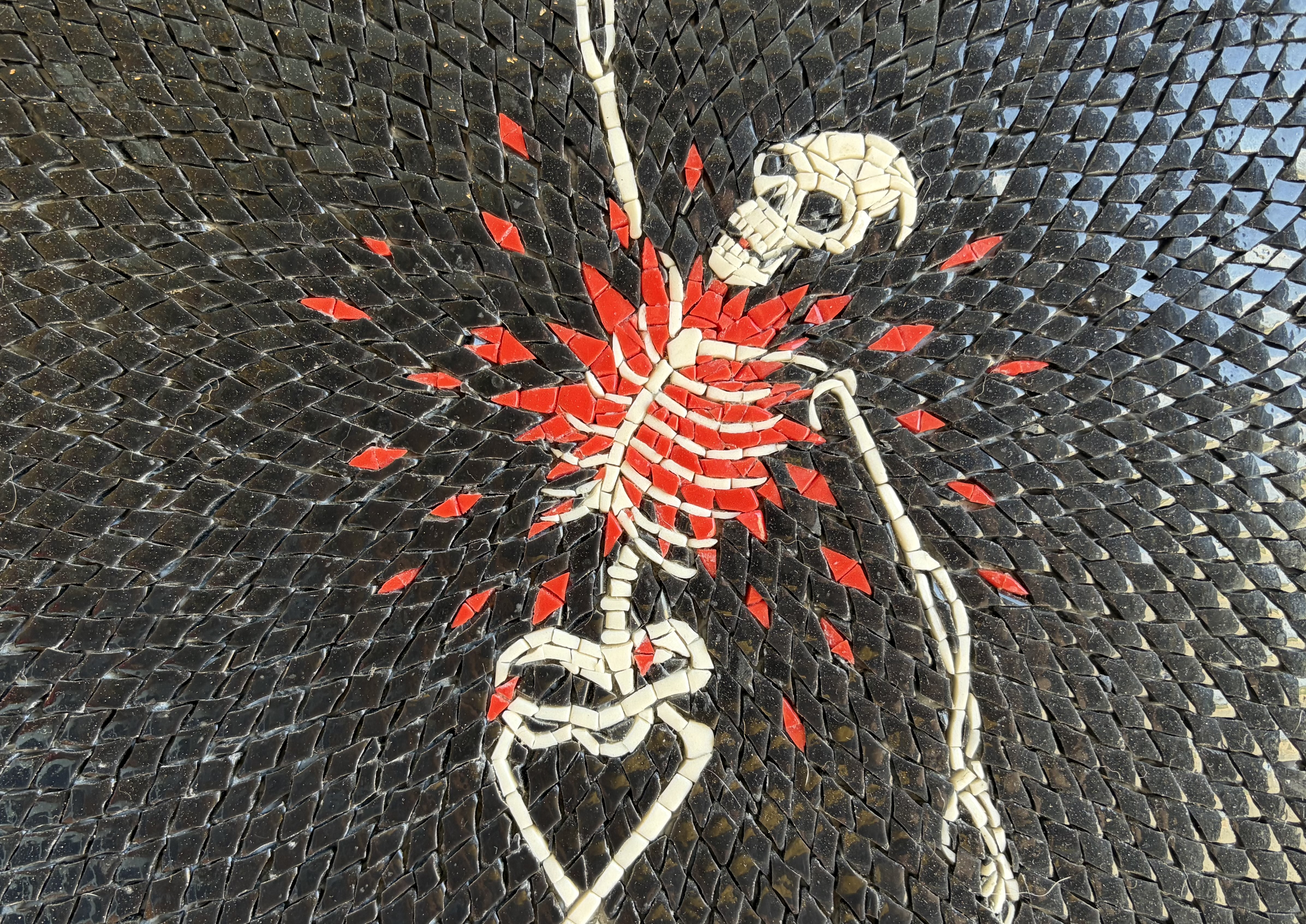 Mosaic skeleton with a bursting red-shard heart on black tesserae