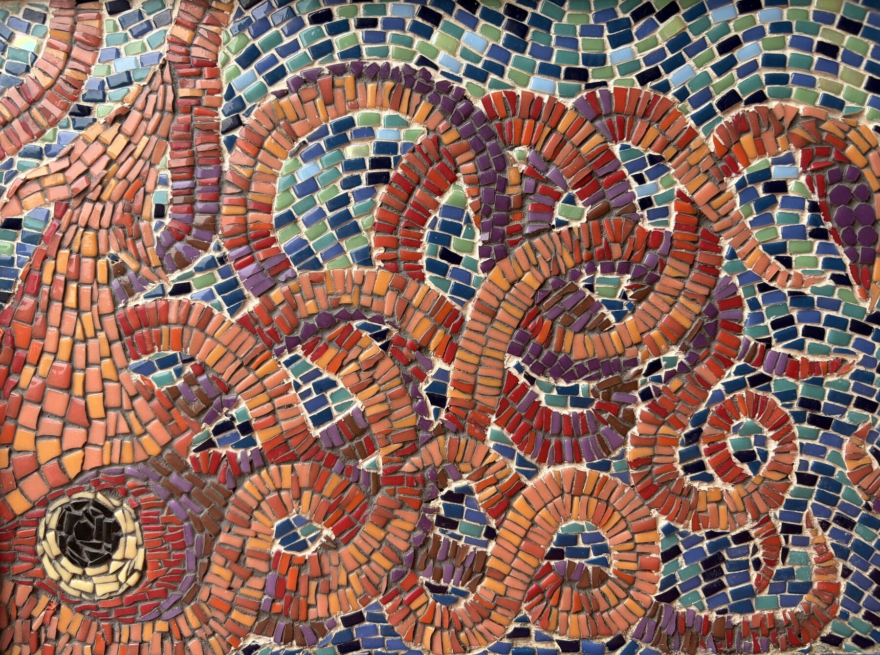 Mosaic detail of interlocking spirals in red, orange, purple, and teal